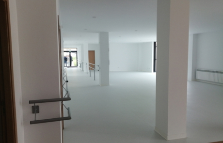 interior de un centro de día, sin mobiliario y pintado en color blanco, en la entrada se ven varias personas