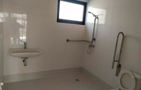 baño de un centro de día con un inodoro para personas con movilidad reducida, un lavabo y la ducha