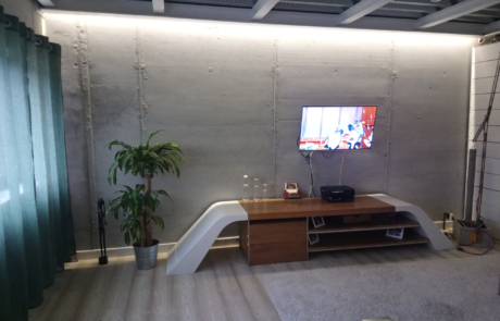 salón de una vivienda con un pequeña estantería y la televisión encendida colgada de la pared