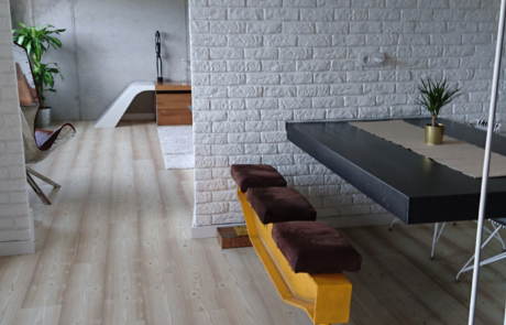 vista de dos zonas de una vivienda, hay una mesa de comedor y al fondo en la otra zona un sillón, una alfombra blanca