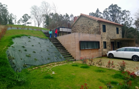 dos niños desde la terraza ajardinada superior de una vivienda, se ve la fachada de piedra y un coche aparcado en la entrada