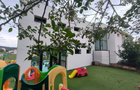 Zona exterior ajardinada de una guardería, se puede ver un pequeño tobogán