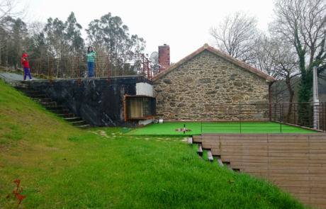 dos niños desde la terraza ajardinada superior de una vivienda, se ve el lateral de piedra de una parte de la fachada.