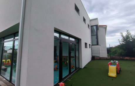 fachada de una guardería, se puede ver la zona del jardín con un pequeño tobogán