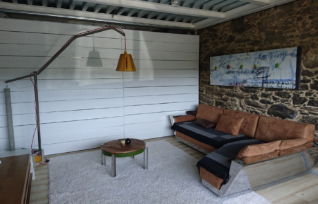 salón de una vivienda con pared de piedra, un sofá grande en color marrón, una lámpara una pequeña mesa