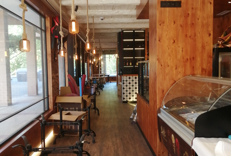 El El pasillo en madera tanto el suelo cómo las paredes, se ven mesas y y el mostrador refrigerador de comida